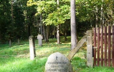 kamkień z krzyżem i napsaem 1914-1918 cmentarz wojenny, w tle  ogrodzony drutem kamienny krzyż i las
