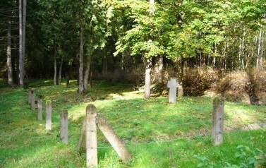 kamienny krzyż, trawa ogrodzone drutami na betonowych słupkach w tle las